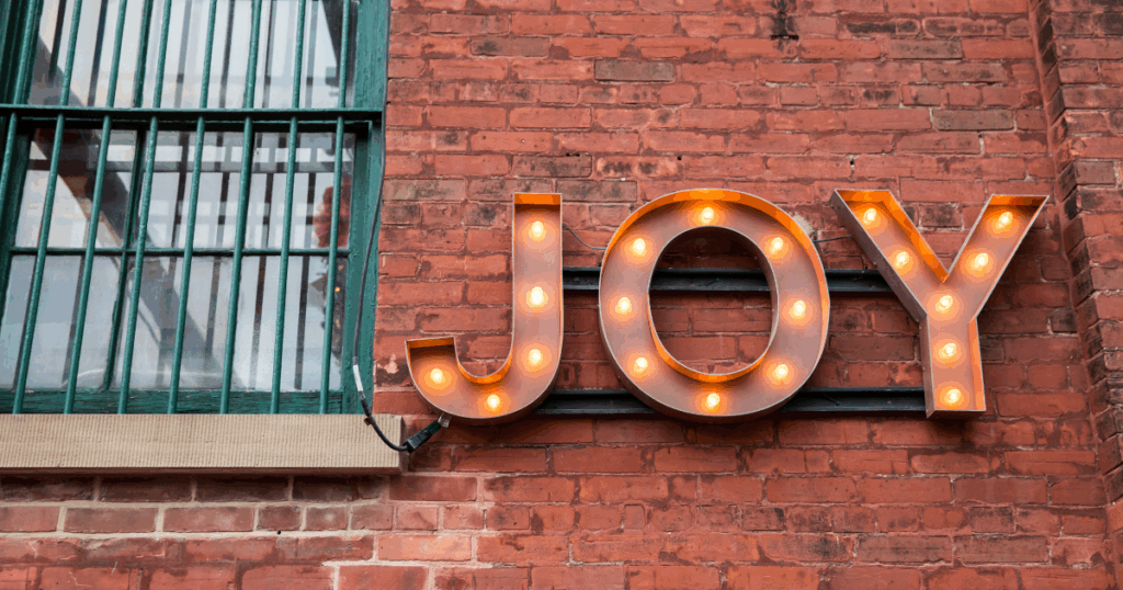 A glowing sign that says "Joy" on a brick wall